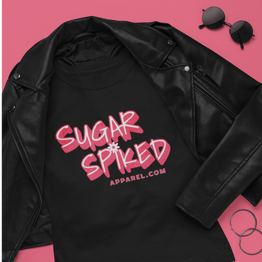 “Flat lay of a black Sugar Spiked Apparel graphic tee styled with a leather jacket, sunglasses, hoop earrings, and studded clutch.